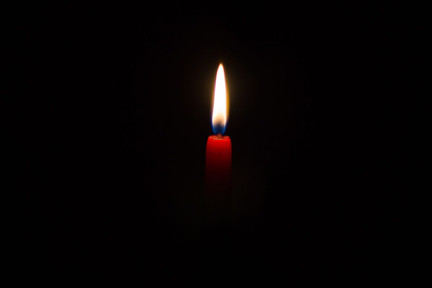red candle with a lit flame against a black background