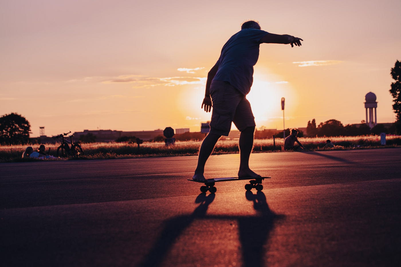 An overweight  man rides a skateboard as the sun sets in the distance.