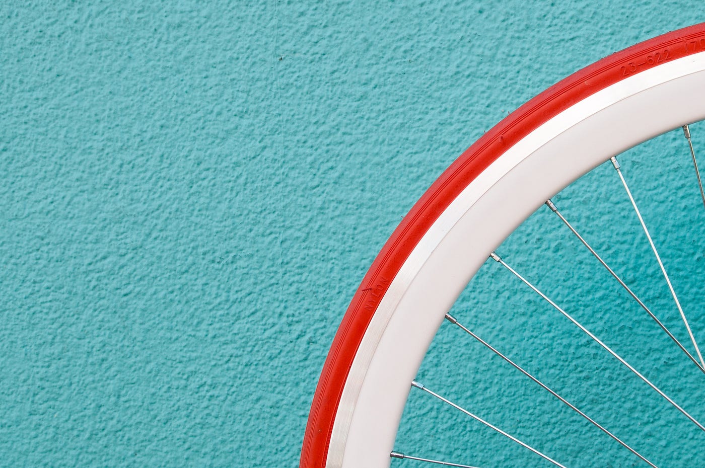 We see the upper rear part of a bicycle tire, with the rim white with a red border. There is a light blye textured background.
