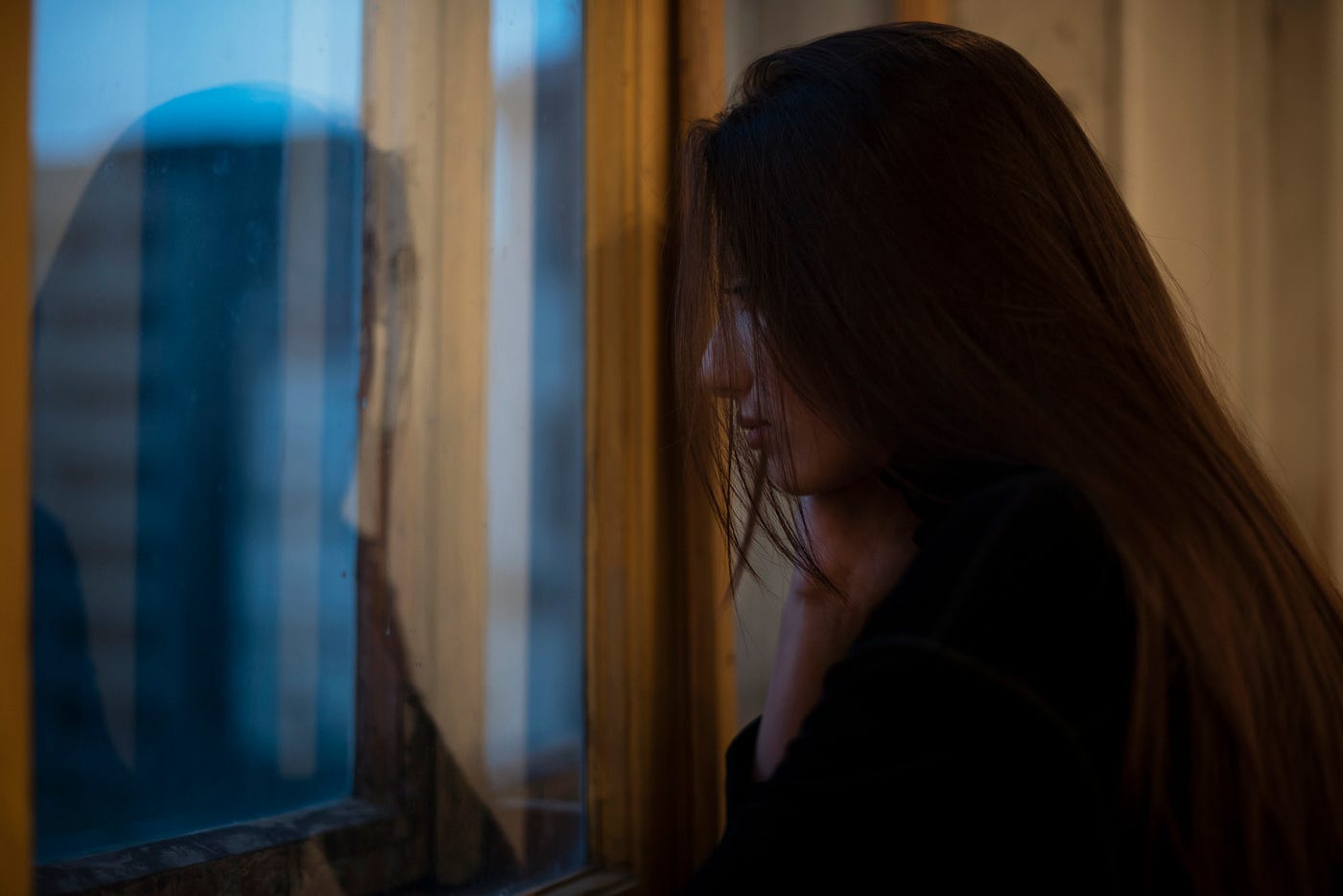A photo of a sad woman with long hair looking out the window.