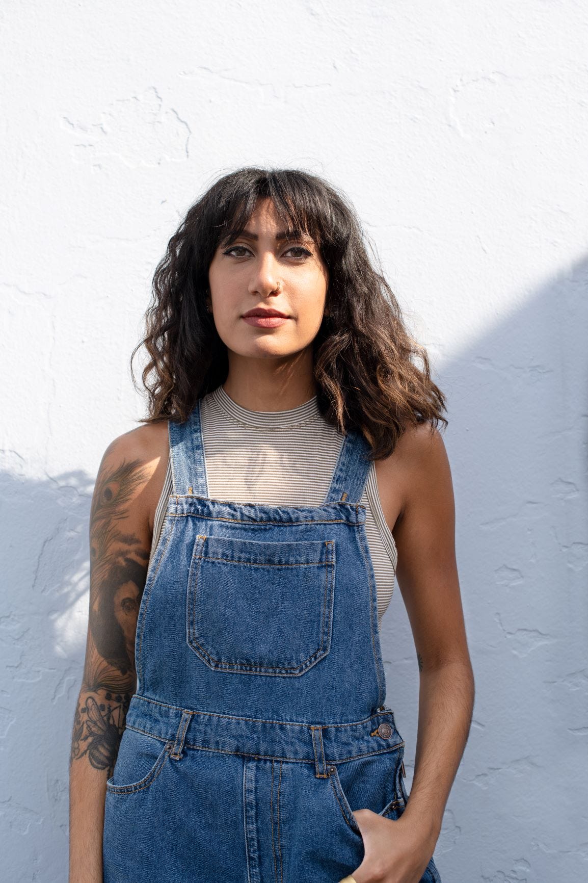Photograph of Jude Abu Zaineh, who has shoulder-length brown hair, dark brown eyes, and a slight smile. She is wearing light blue overalls and looks steadily at the camera.