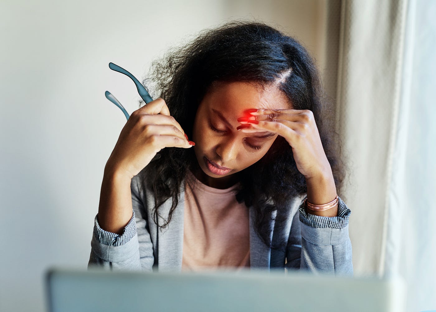 Shot of a young woman suffering from a headache while using a laptop at home.