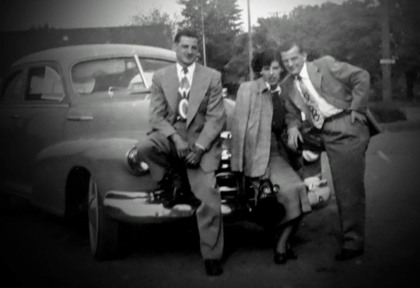 Two young men and a woman posing at the front of a car in 1940.