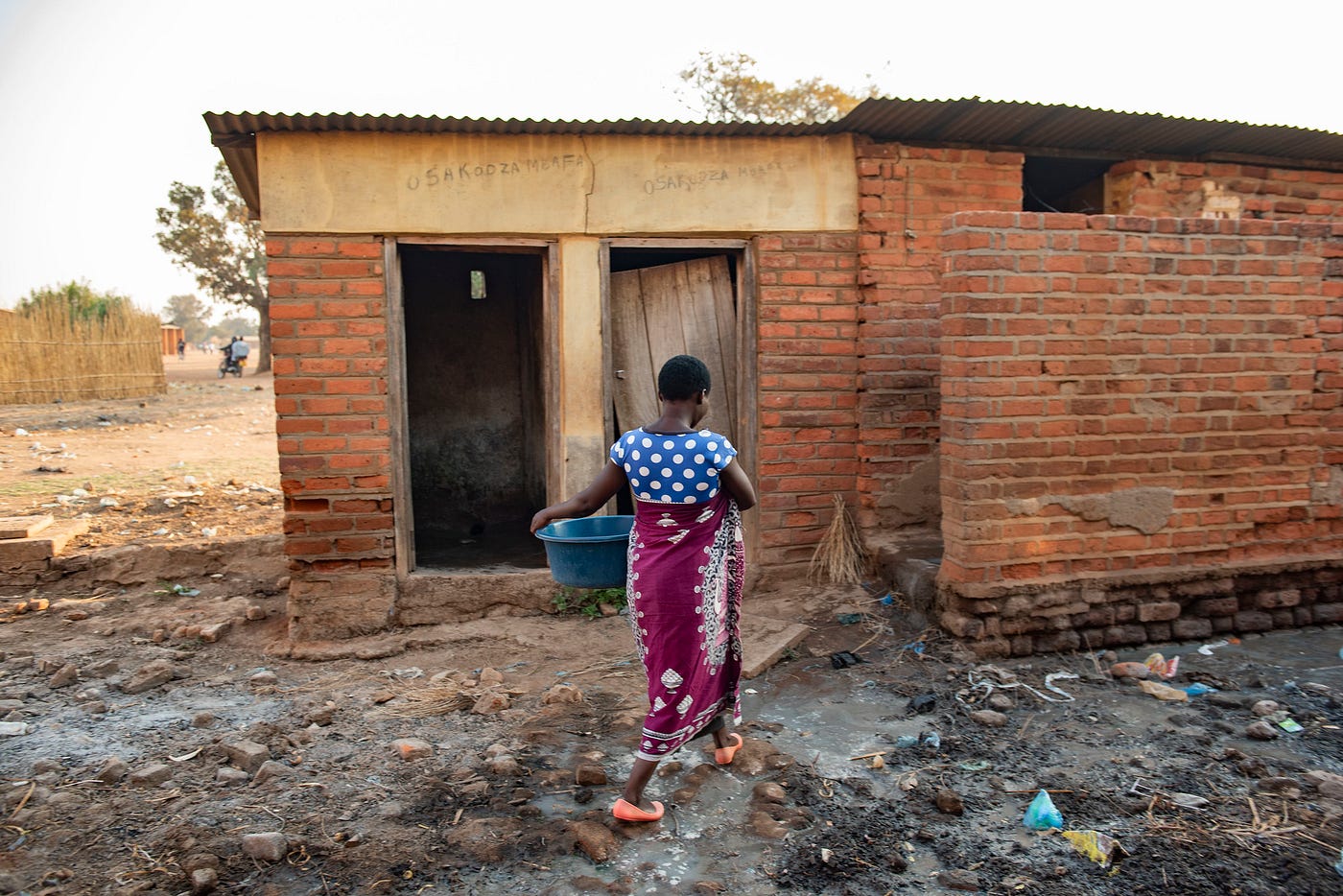 A Malawian woman makes her way through a cluttered pathway on her way to a inadequate toilet facility at a health center.