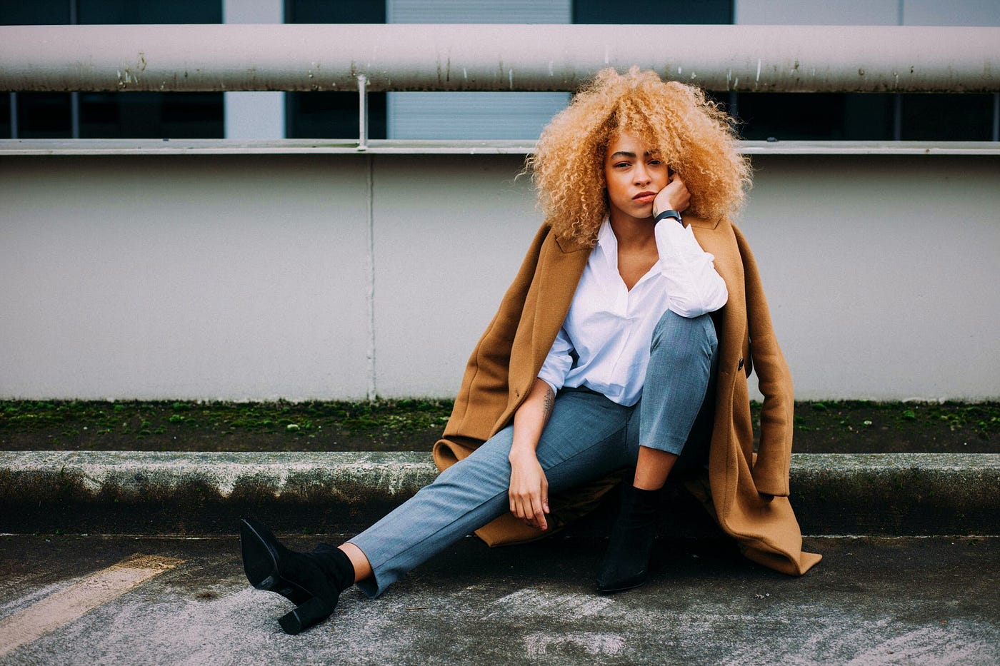 unhappy woman wearing white shirt and blue jeans sitting on concrete with hand on her cheek