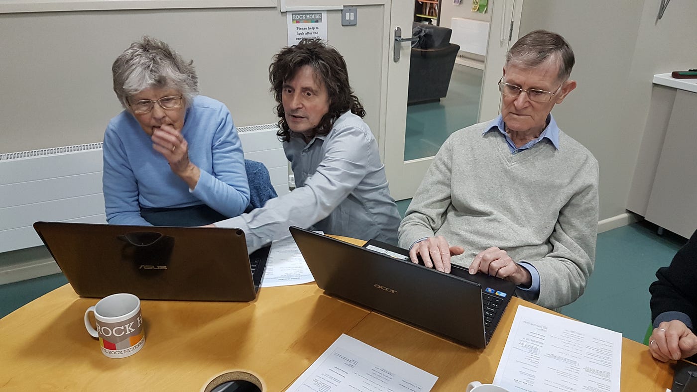 shows a man in the centre of three people looking at two laptops