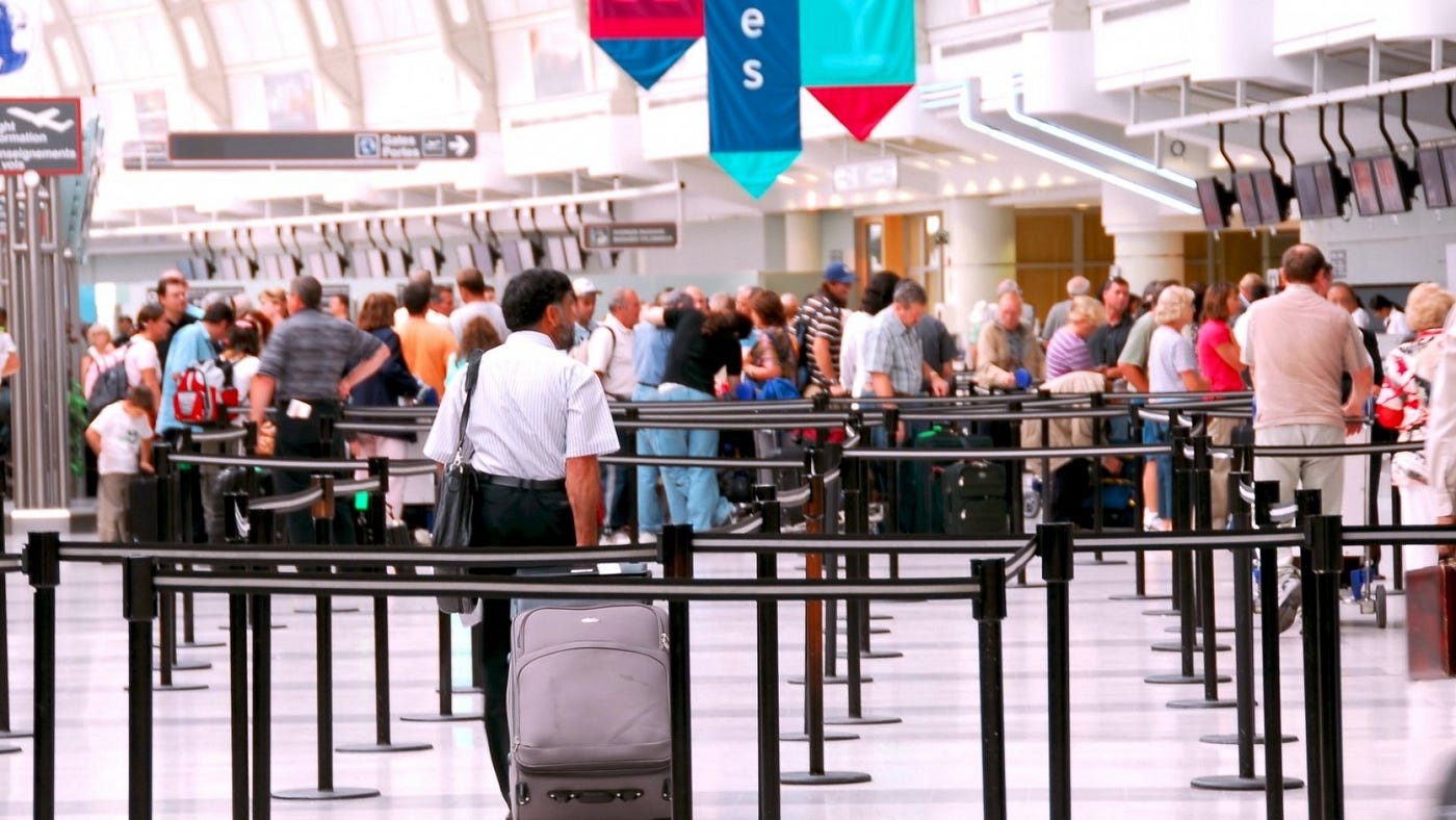 Travelers with suitcases waiting in check-in line at a large airport.