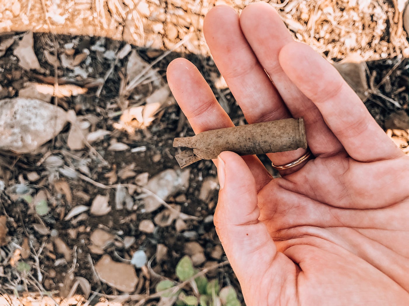 A hand holds a rusting bullet casing over the ground.