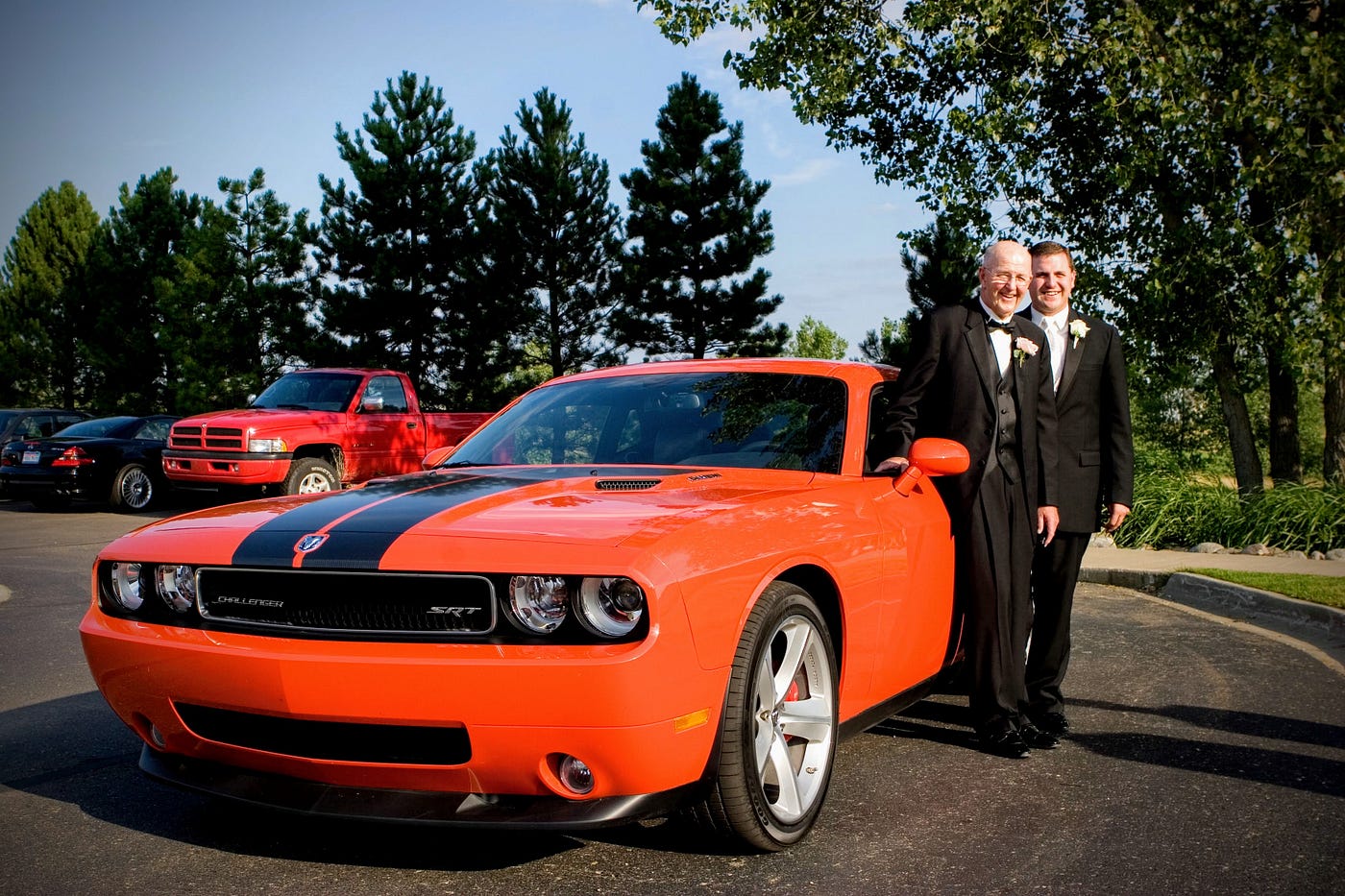 Father and son wearing tuxedos standing next to their new Orange and Black Dodge Challenger SRT-8.