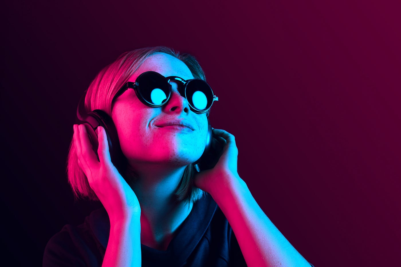 A photo of a girl with sunglasses and headphones on, with neon pink/blue lighting.
