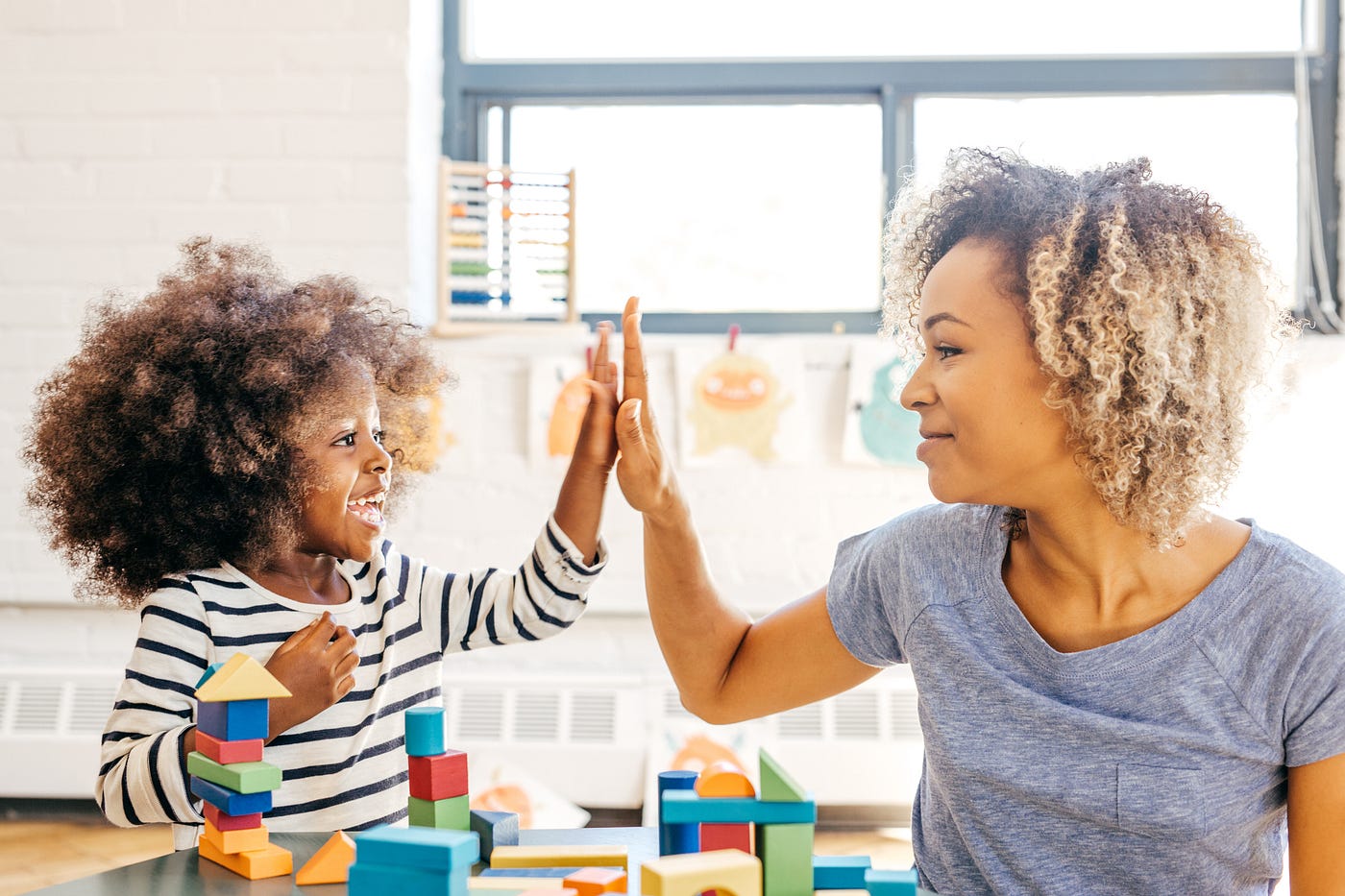 A photo of a mom and her young child high fiving as the kid plays with blocks.