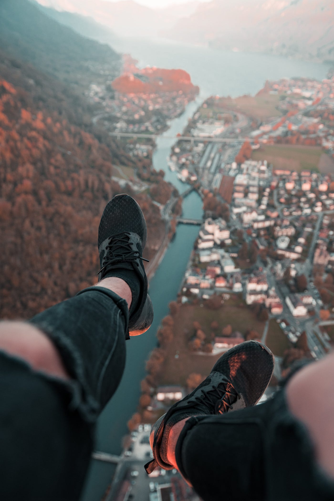 Man dangles feet over cliff looking down onto a city