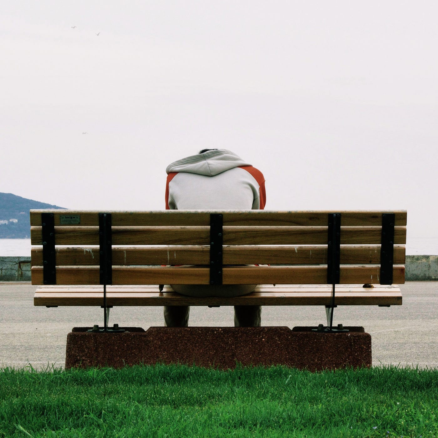 A man sits on a bench looking out to sea with his head bowed