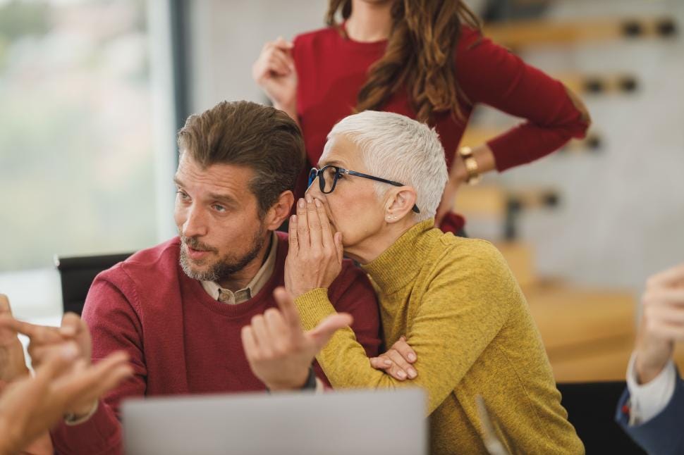 Woman whispering into a man’s ear at work