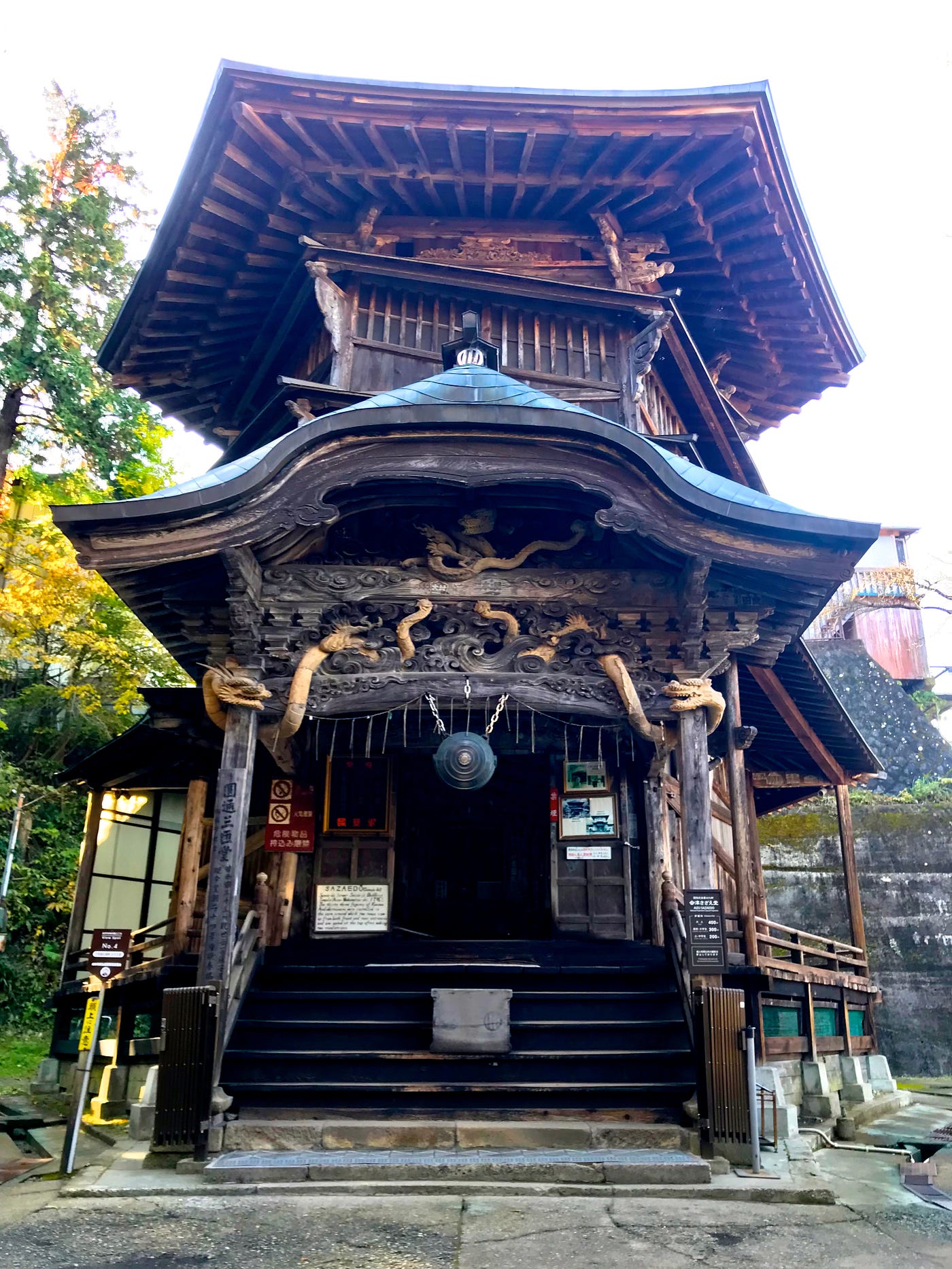 Hexagonal, 3 story, old wooden building, with intricate dragon and other carvings, as well as a brass gong above the entrance. Its roof extends out, showing the wooden beams beneath.
