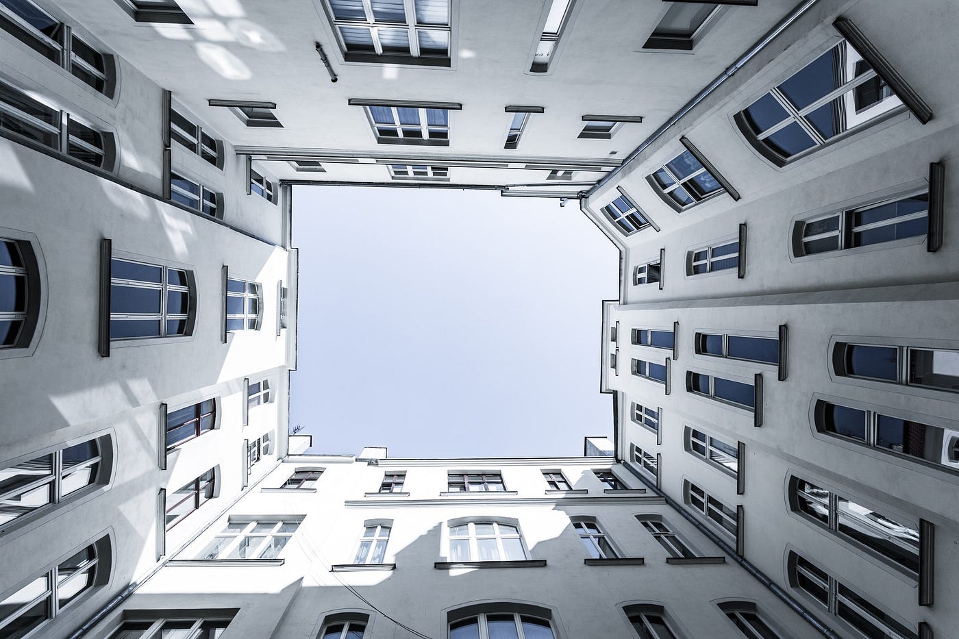 A square of clear light-blue sky framed by three or four stories of four off-white walls full of windows. (The sky might have a layer of white cloud cover but it’s uniform.)