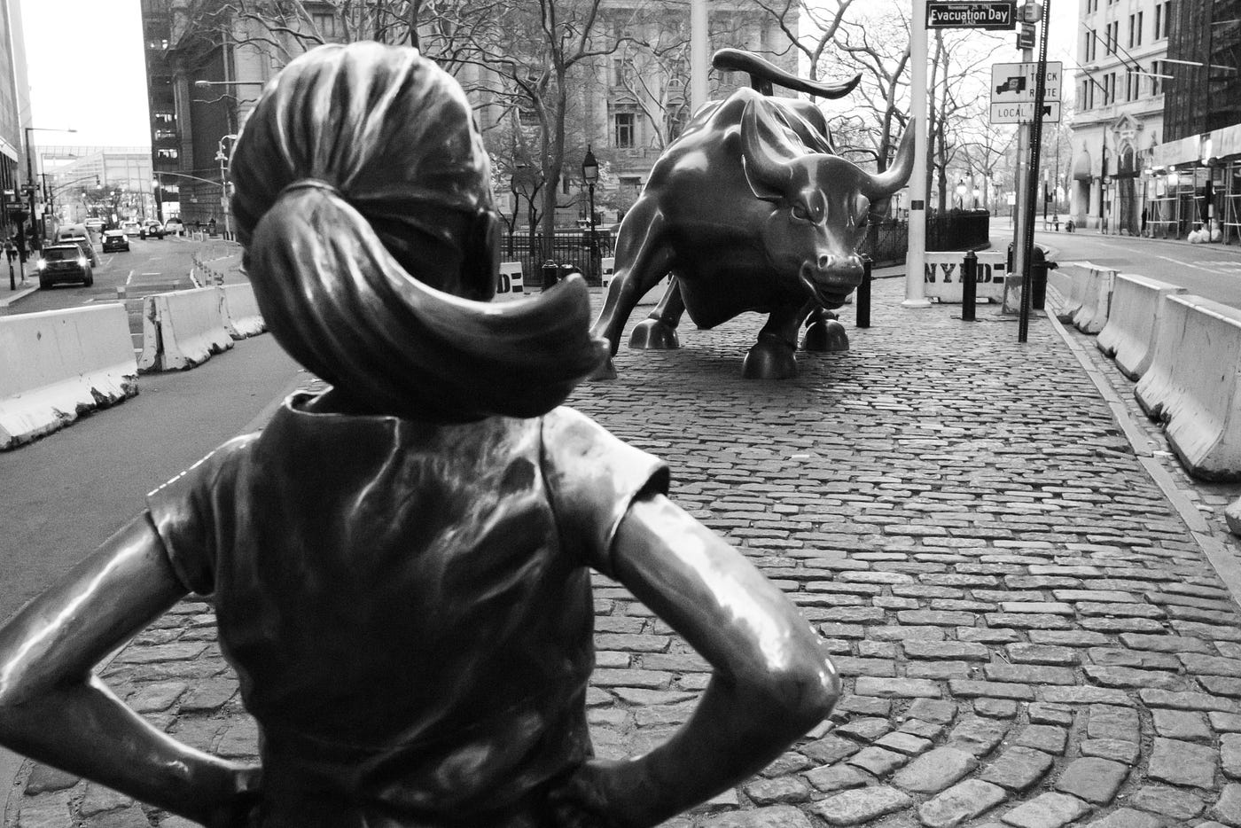 Statue of girl facing Wall Street bull on street.