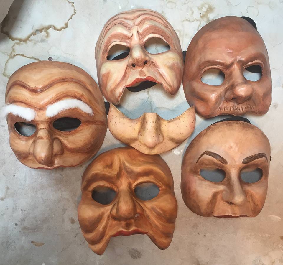 5 three quarter contemporary commedia masks of varying skin tones, one with very bushy white eyebrows, and one just across the nose and cheek mask in the center.