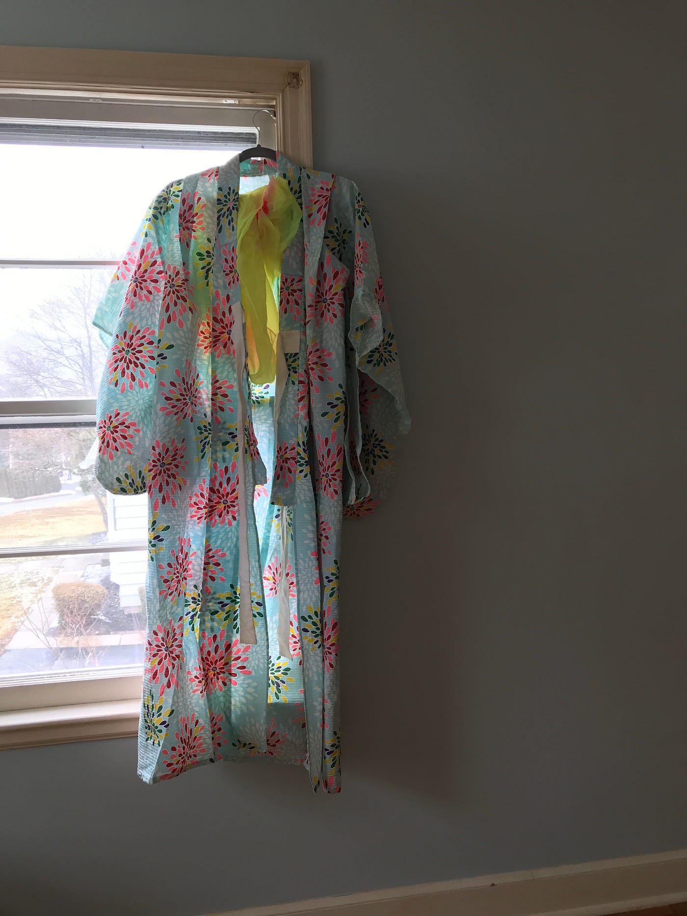 A blue robe with splashes of color hangs from the sill of a window.