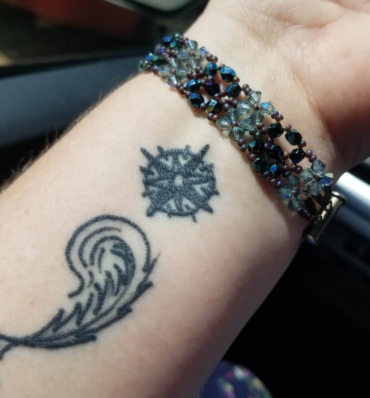 woman’s wrist with a tattoo of a compass and writing quill in the form of a semi-colon which is a symbol of mental health awareness a symbol meaning “you continue.”