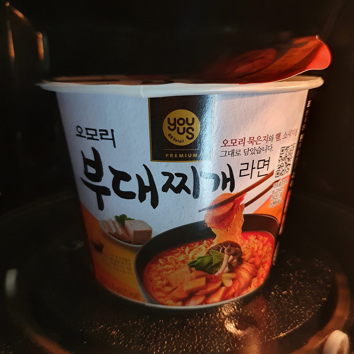 A cup of YouUs Omori Budae-jjigae Ramen in the microwave cooking for 3 minutes and 30 seconds.