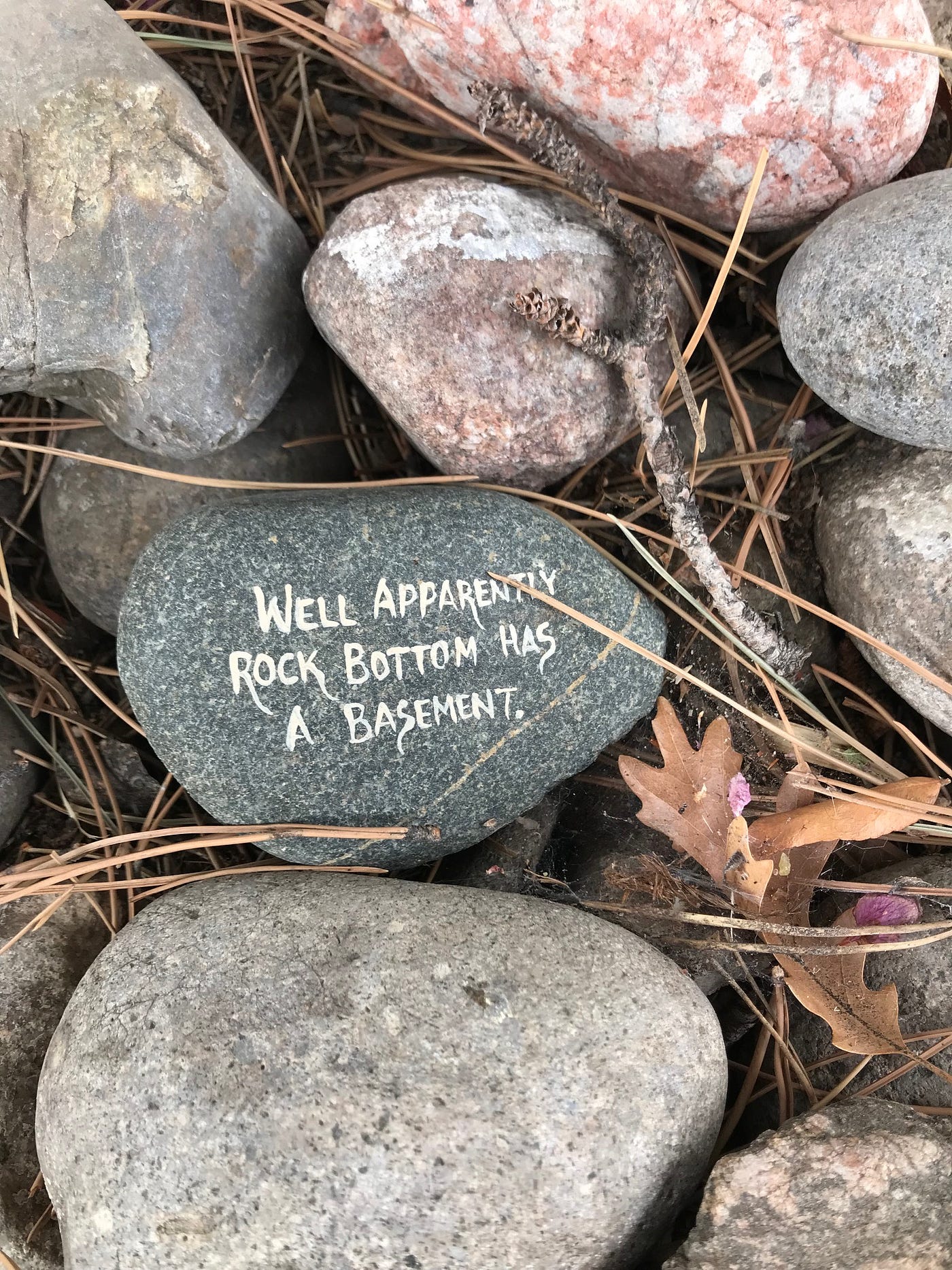 A rock with “Well apparently rock bottom has a basement” written in white paint.