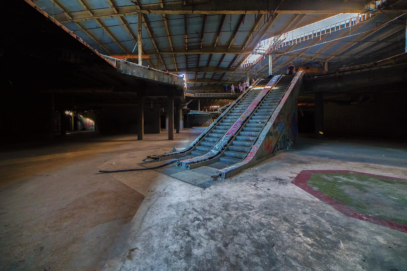 Interior of a dilapidated abandoned mall with escalator and floor tiles prominently featured