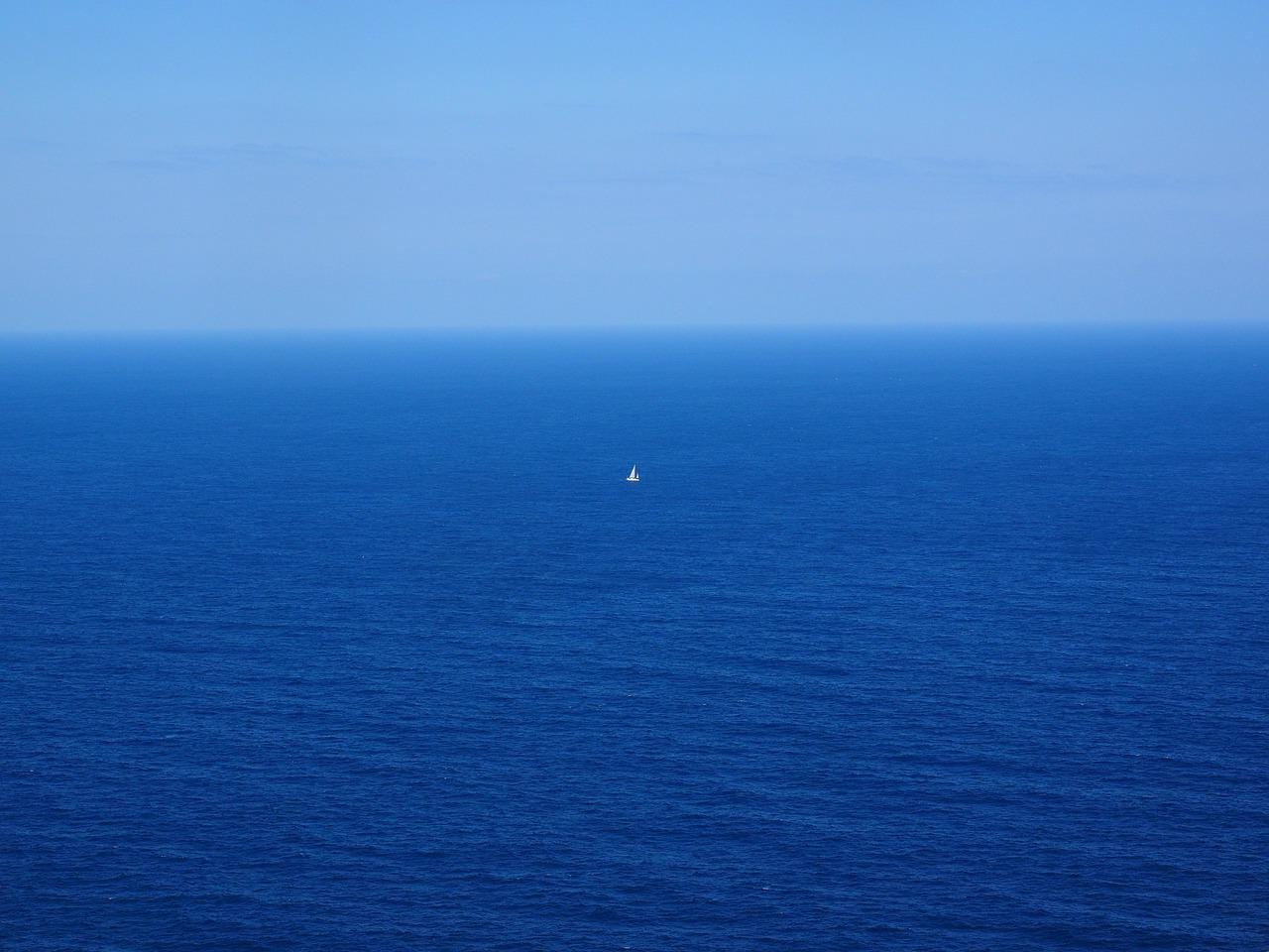 A wide empty ocean with a small white boat far in the distance