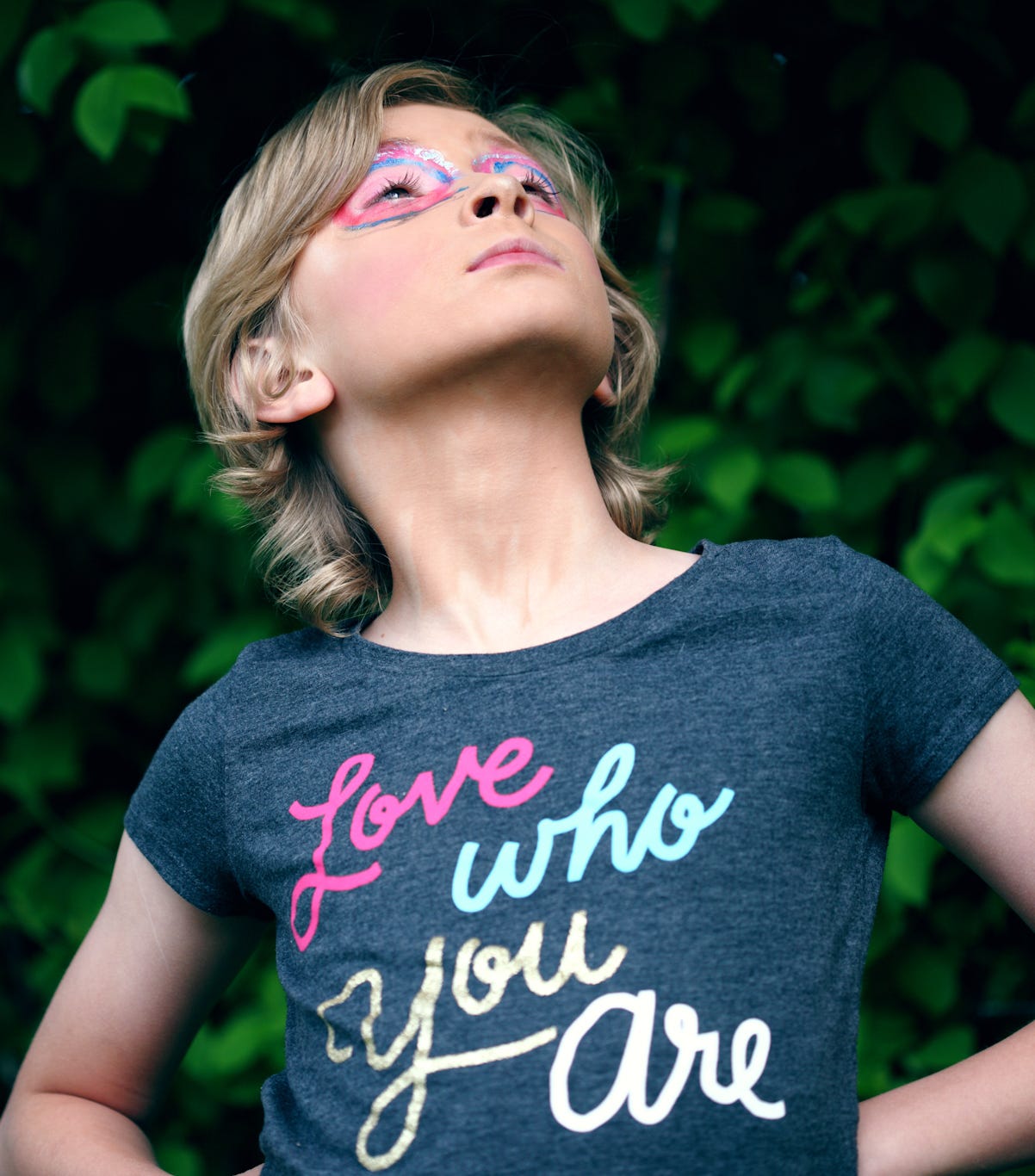 Young woman with colors of the trans flag in eye makeup and wearing a shirt that says “Love who you love”