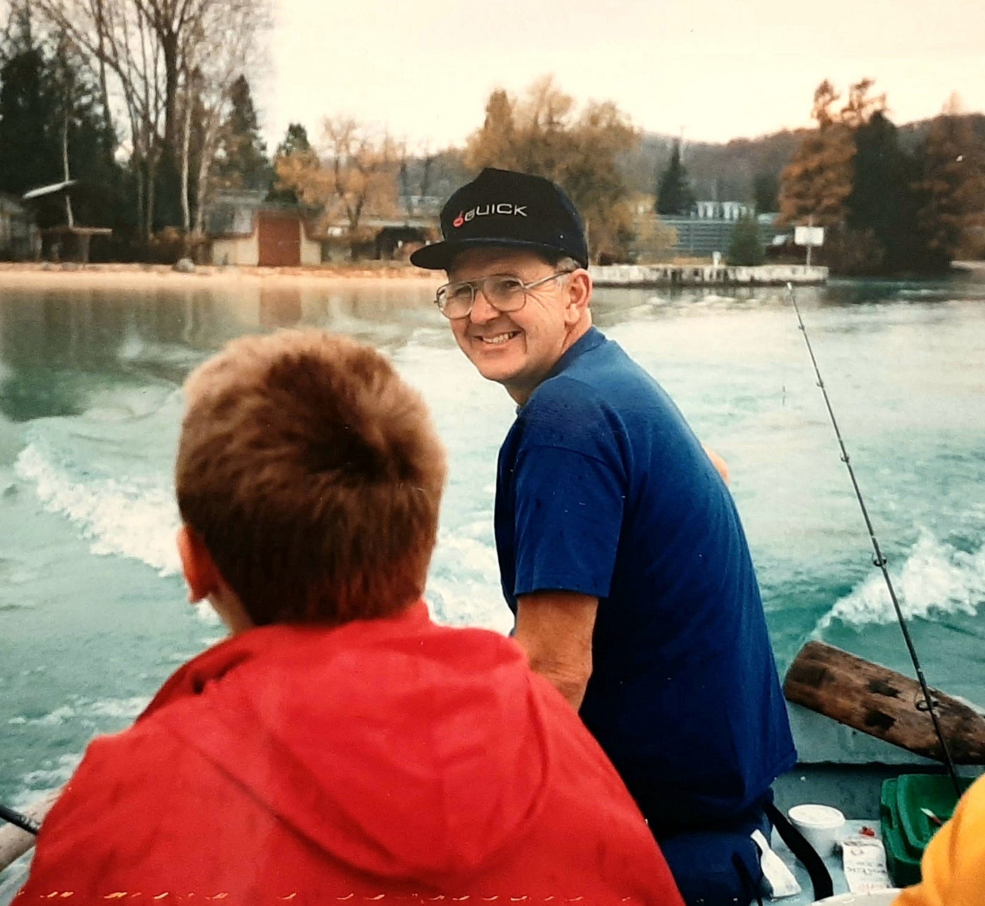 Father driving old aluminum boat on lake with son sitting in front.
