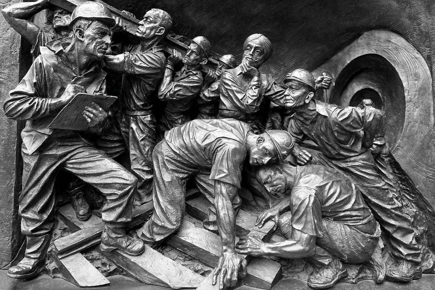 Embossed silver sculpture of several men constructing a railroad with one man in the middle staring off into the distance, contemplating.