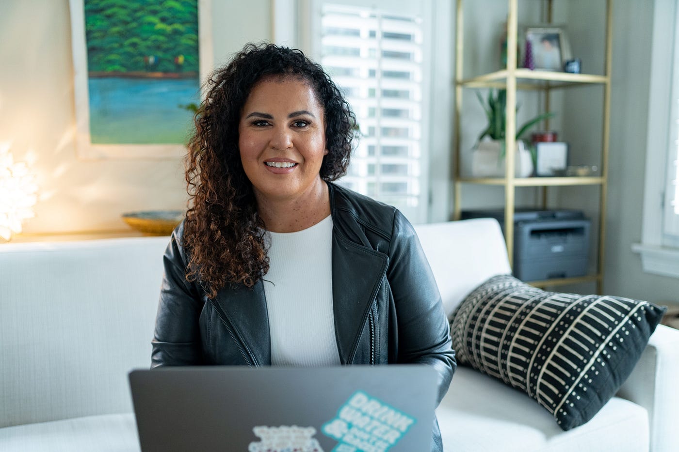 woman in leather jacket seated at table with mac laptop