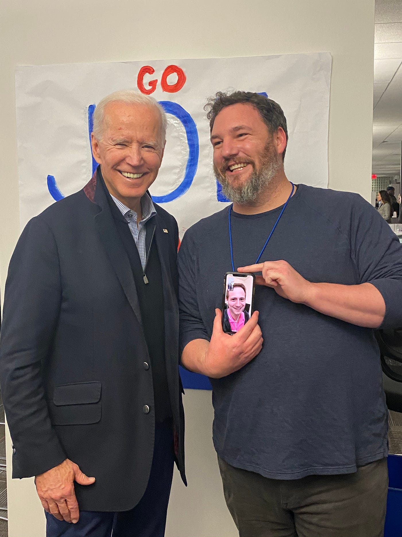 Joe Biden stands left of Dan Woods. Dan is holding his phone with Matt on the screen to meet the boss.