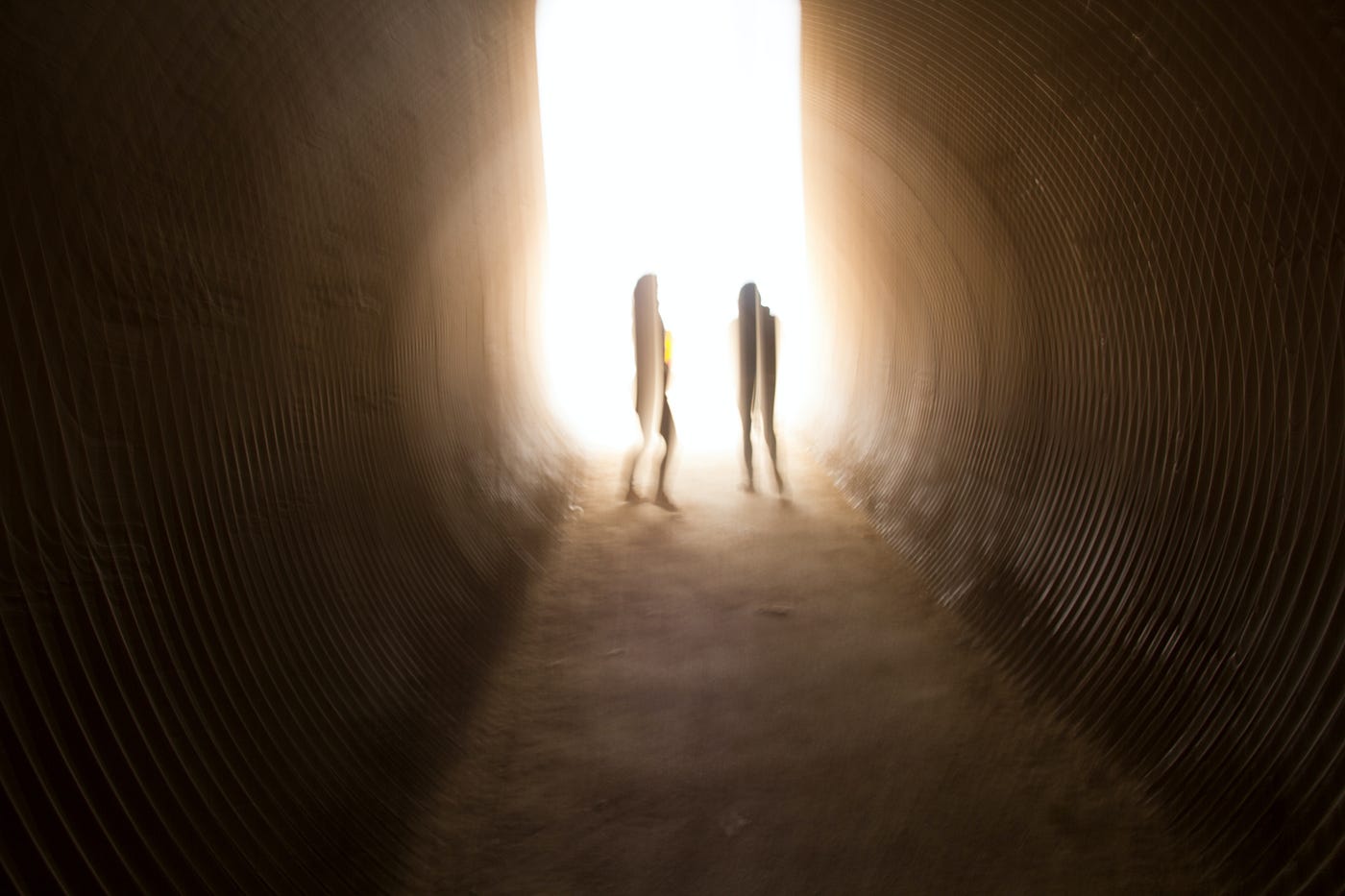 Sepia-toned photo of two people standing towards the end of what appears to be a tunnel, with light shining at the end