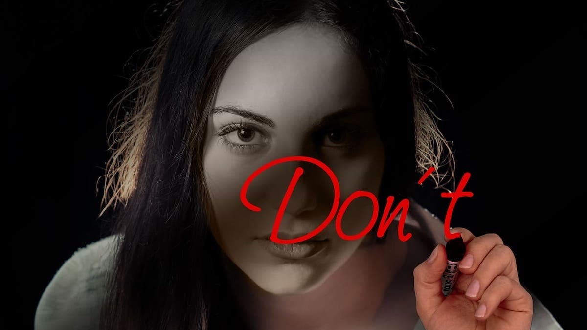 A woman writing the word Don’t in red lipstick on a window