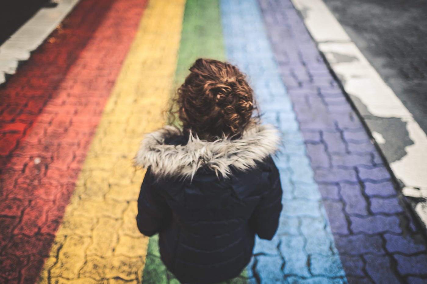 Kid seen from the back, walks on a rainbow-painted crosswalk