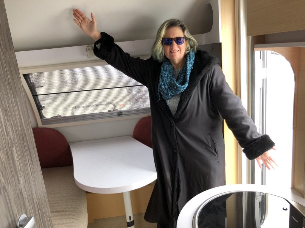 Stacey in tiny teardrop camper showing with her arms how small the space is inside.