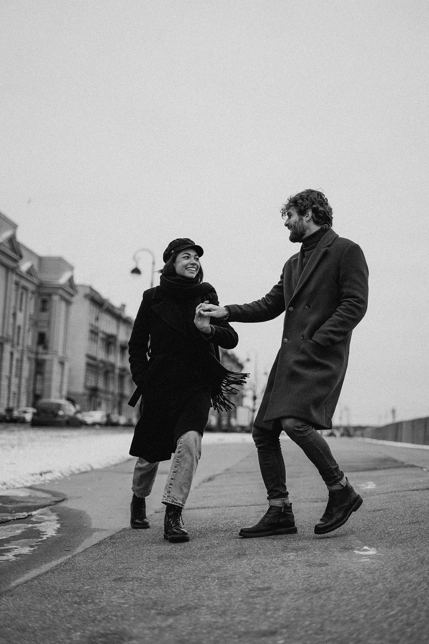 The best relationship advice you’ll ever use. A black and white photo of a loving couple prancing down the street on a cold, grey day. The man takes her hand, as they express joy. The woman’s smile is genuinely captivating.