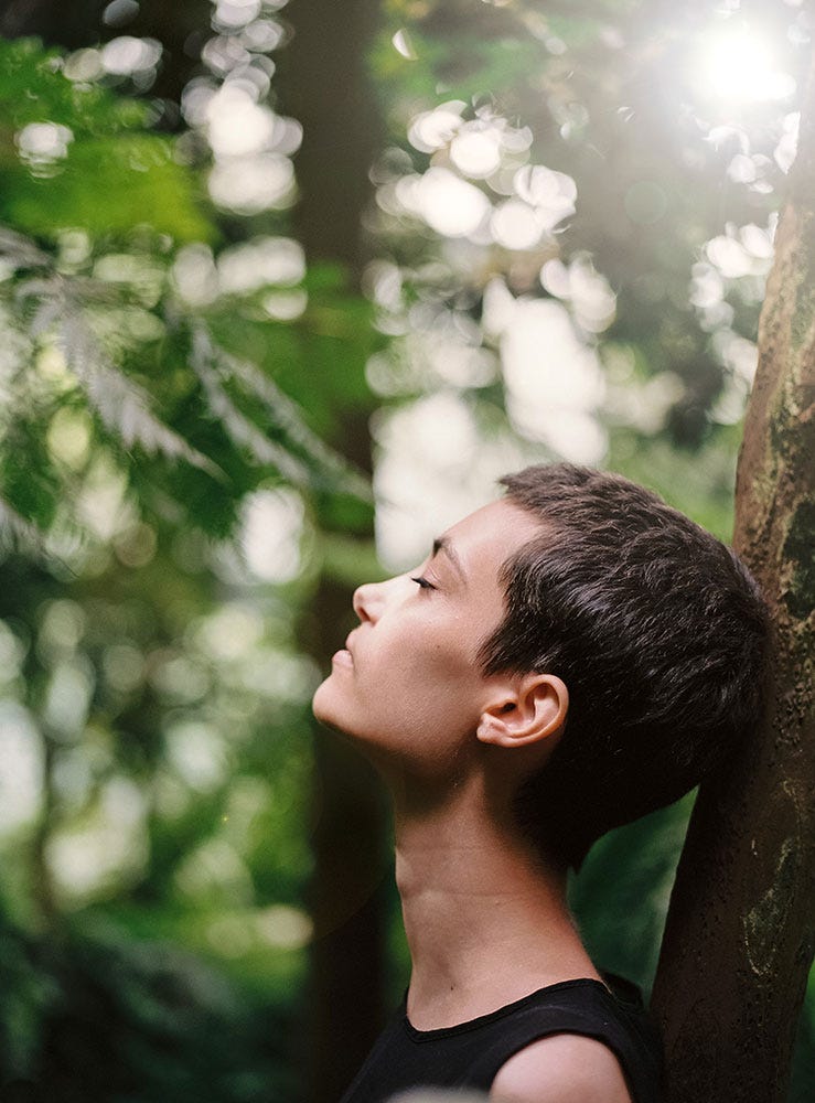 Woman leaning against tree with eyes closed in contemplation.