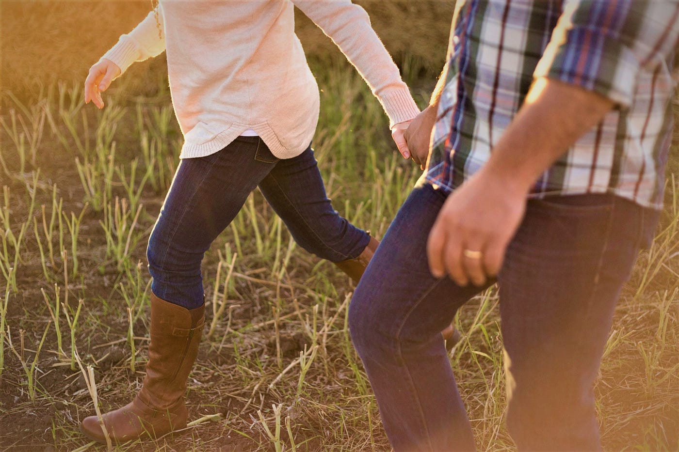 man and woman walking through grassy field holding hands