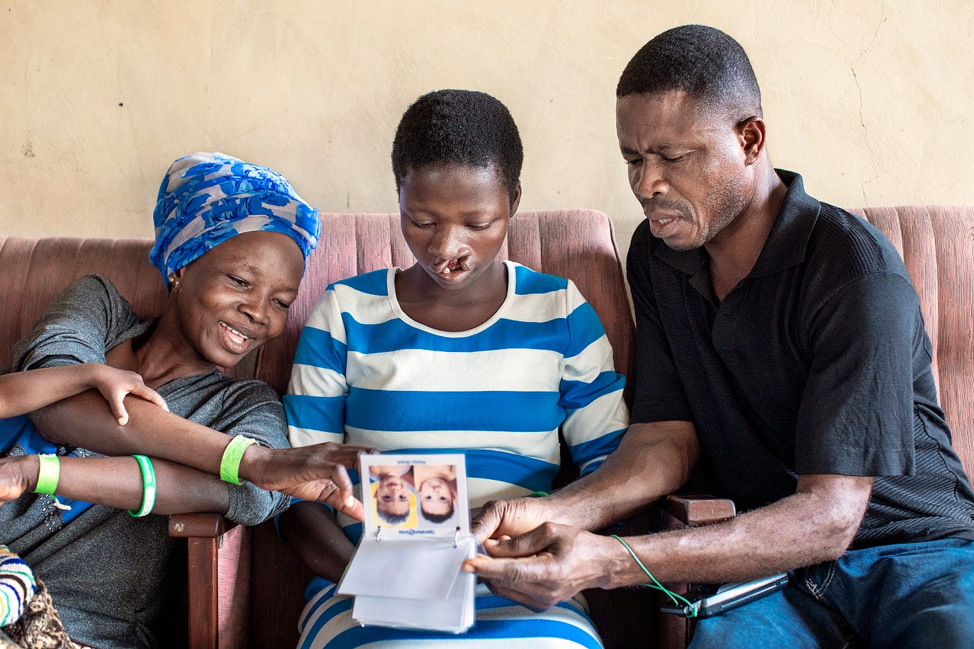 Three people sit on a bench looking at a flip book of photos.
