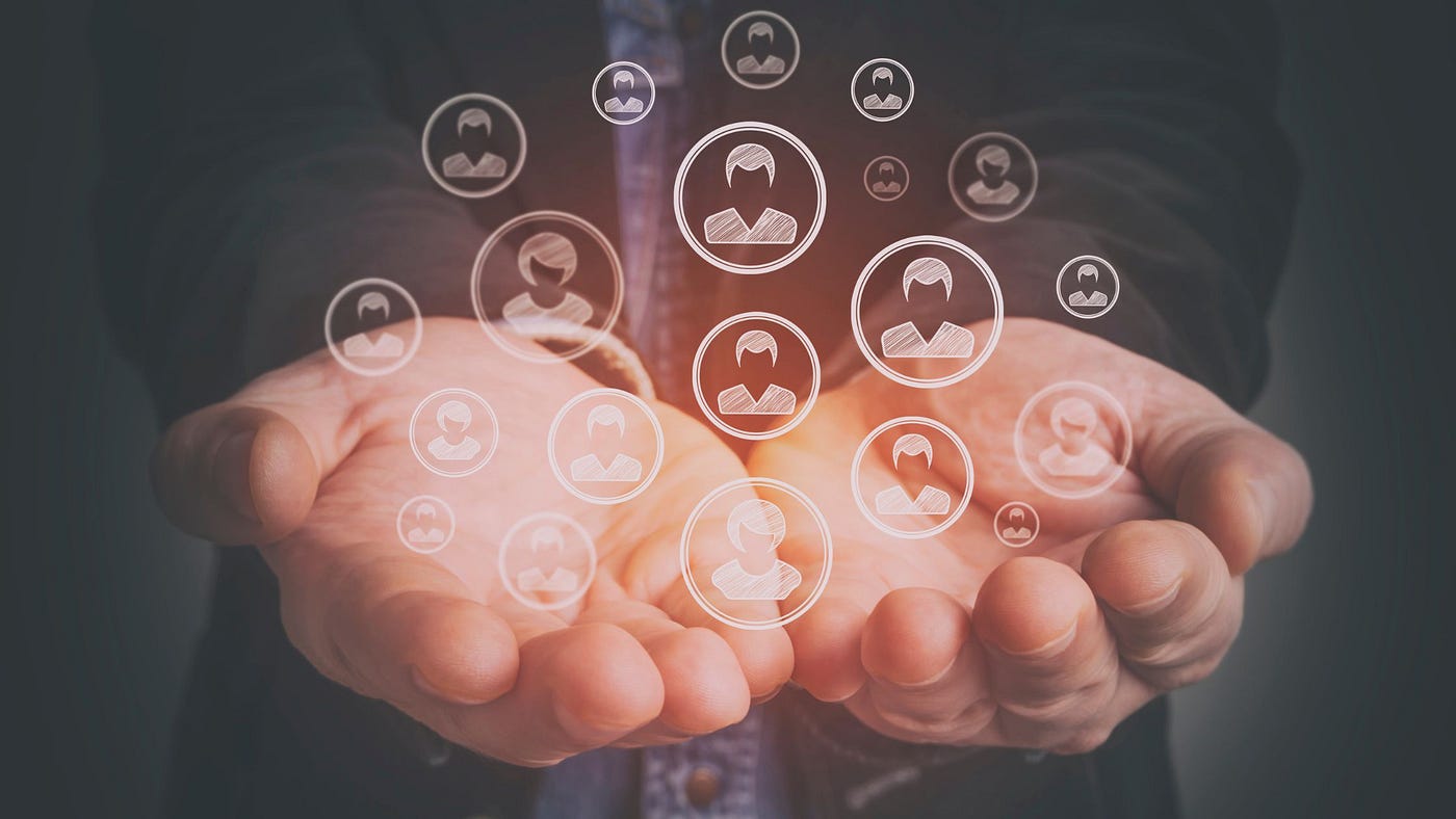 Photo of a person’s hands held out in a bowl-shape, holding a group of abstract people icons of various sizes.