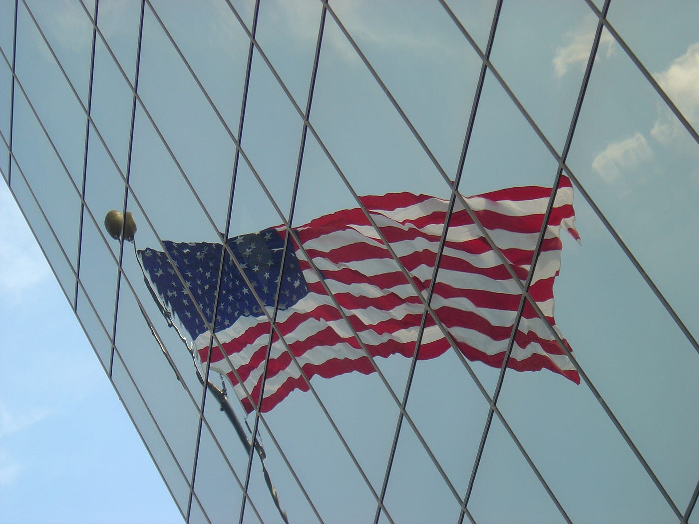 American flag reflected on the glass surface of a building, distorted.