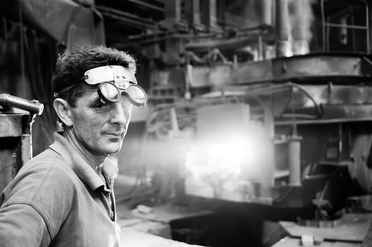 A worker standing in front of an electric arc furnace in a steel mill