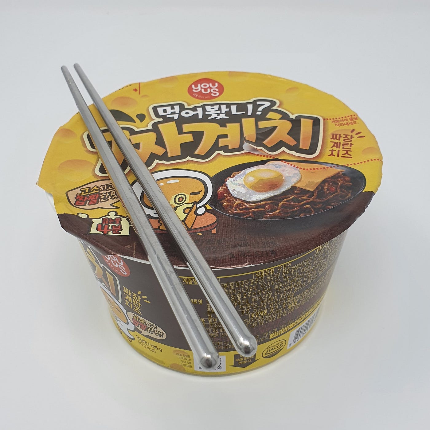 A closed cup of YouUs Jjagyechi Instant Noodles cooking for 4 minutes with chopsticks resting on top.