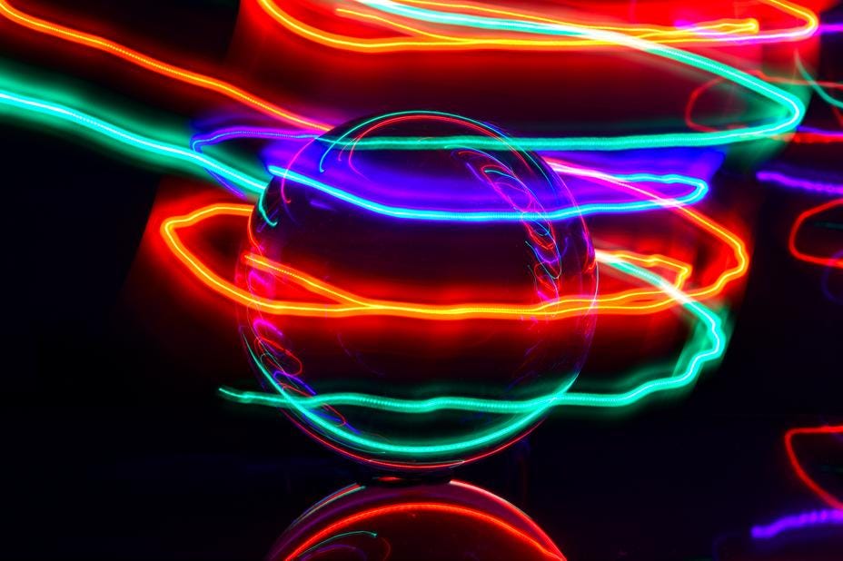 Crystal ball with green, blue, red, and orange rays of light spiraling around it. Black background.