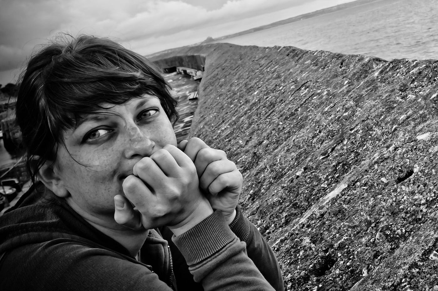 Portrait of me leaning on a sea wall with St Michael’s Mount, Cornwall in the distance. My eyebrows have bald patches.