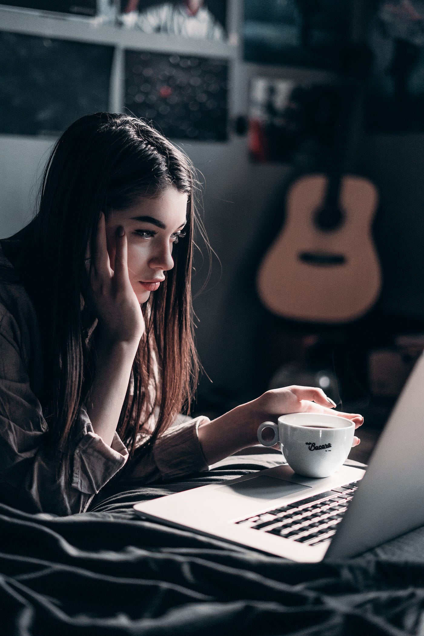 woman on bed drinking coffee and using laptop