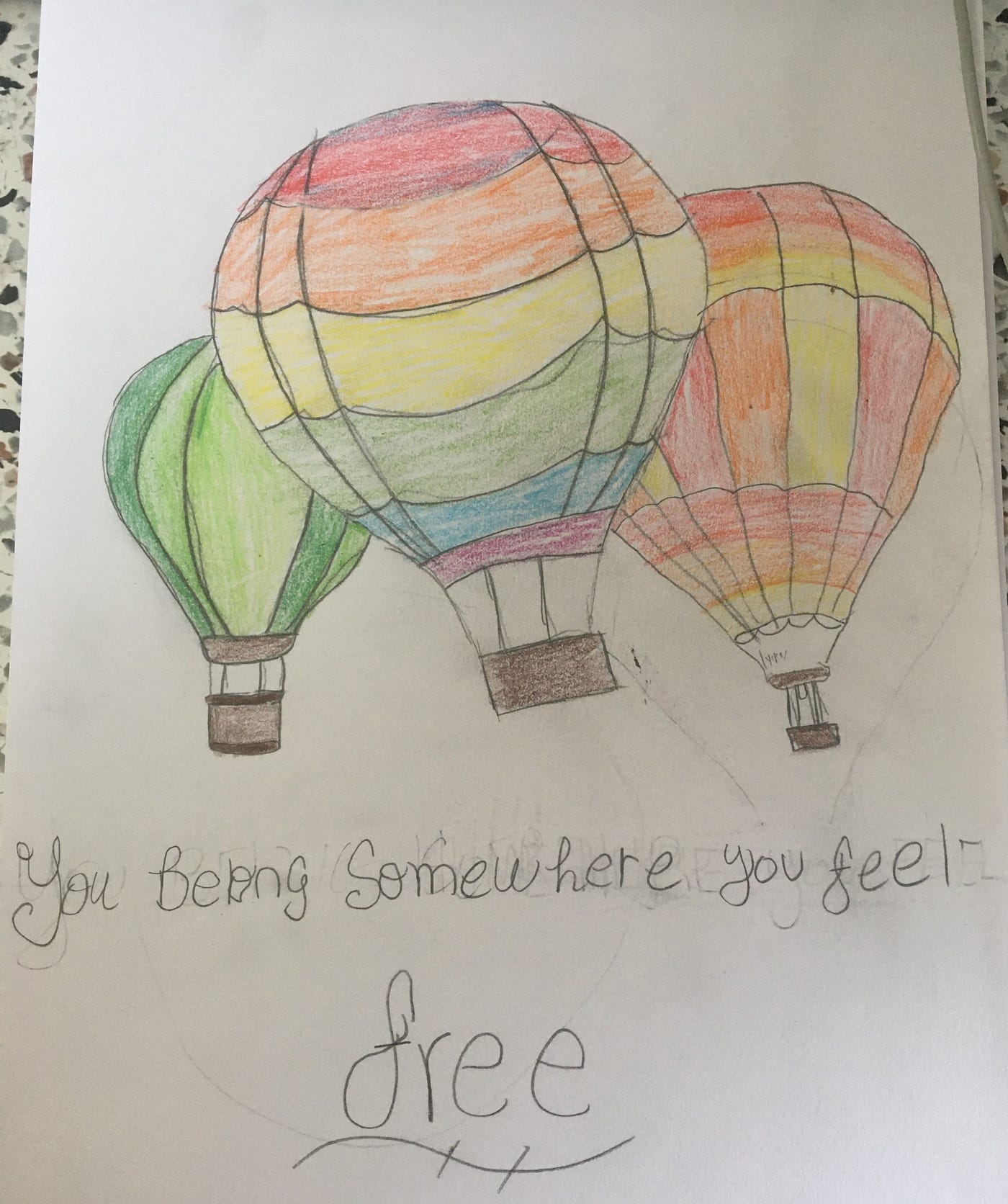 This artwork is a coloured pencil drawing that features rainbow-coloured hot air balloons, and reads: “You belong somewhere you feel free.”