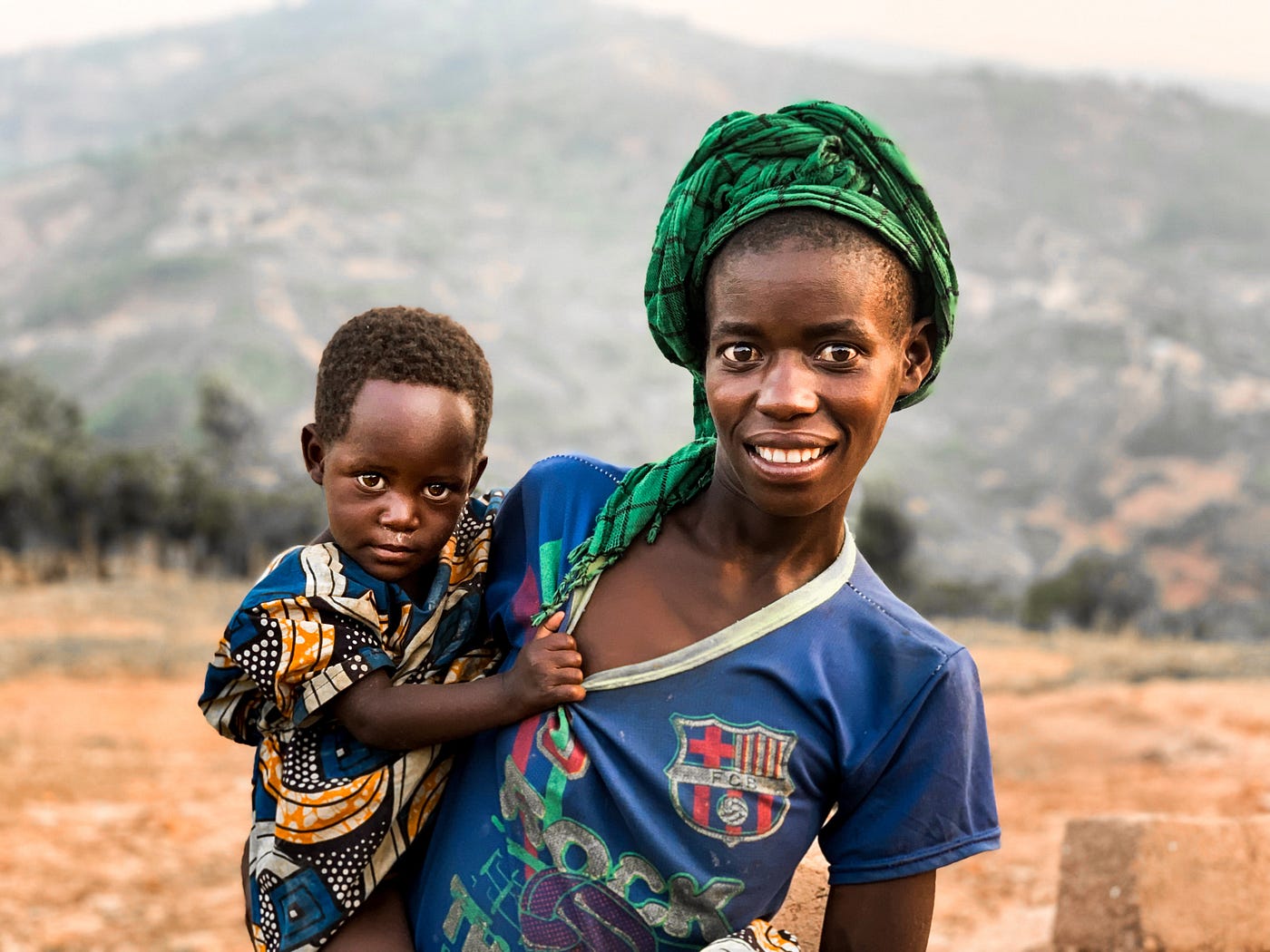 An African mother with her child in hand. They’re both on a dry land.